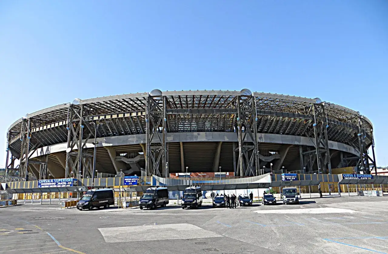Stadion Napoli z widocznymi wejściami i kilkoma samochodami policyjnymi na parkingu.