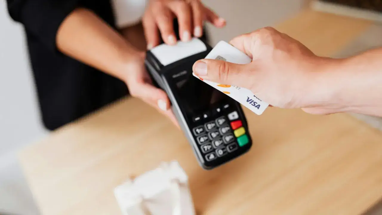 Zbliżenie na rękę zbliżającą kartę Visa do terminala płatniczego.