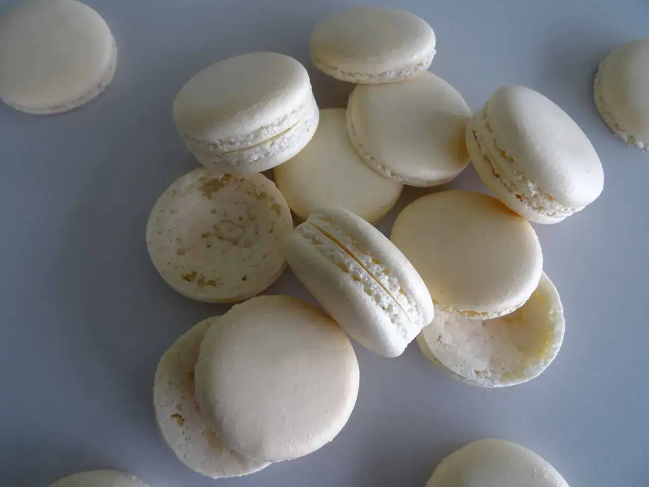 Un tas de macarons blancs, certains assemblés, d'autres séparés, prêts pour de délicieuses recettes de macarons.