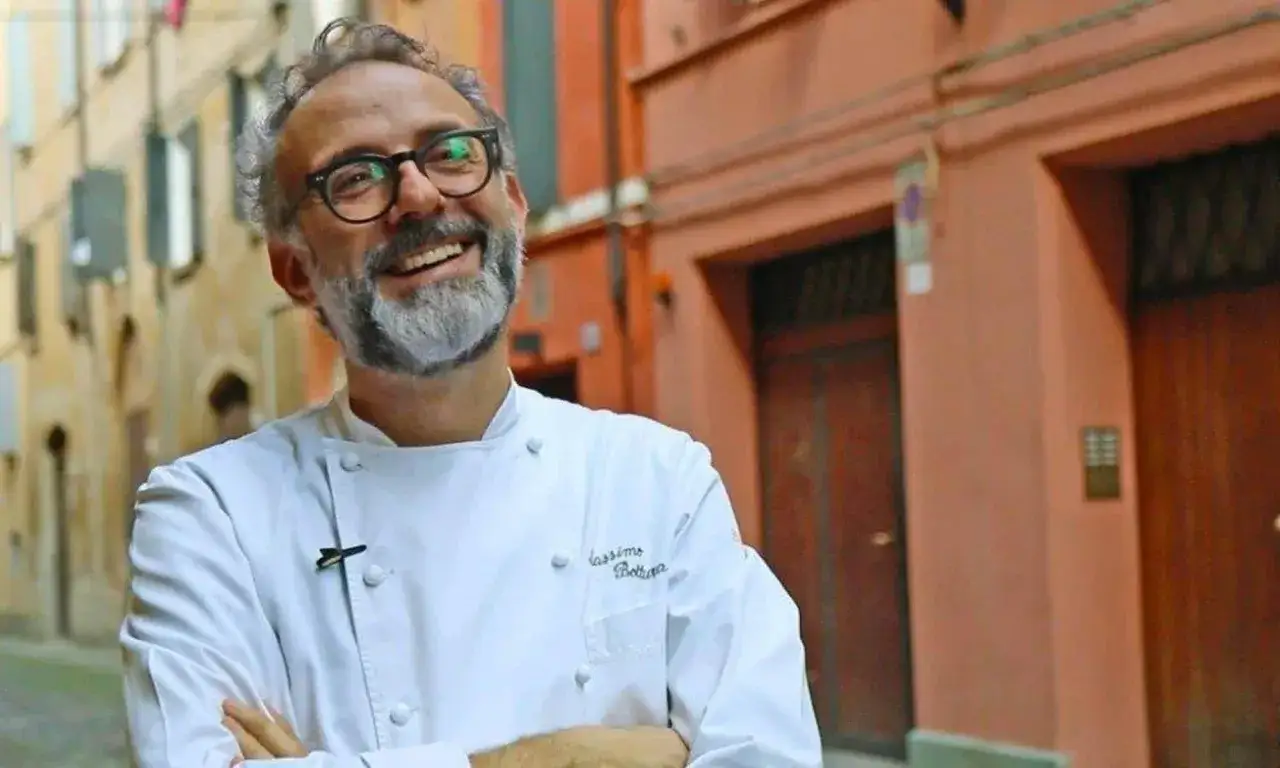 Massimo Bottura, uno dei pi&ugrave; celebri chef stellati italiani, sorride con orgoglio in una strada italiana.