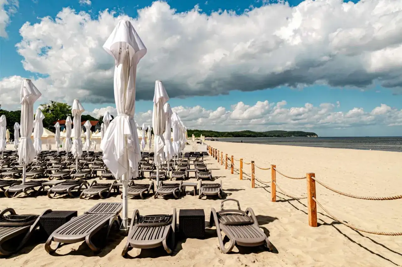 Tomma solstolar och vita parasoller på Sopot beach väntar på besökare under en molnig men ljus dag.