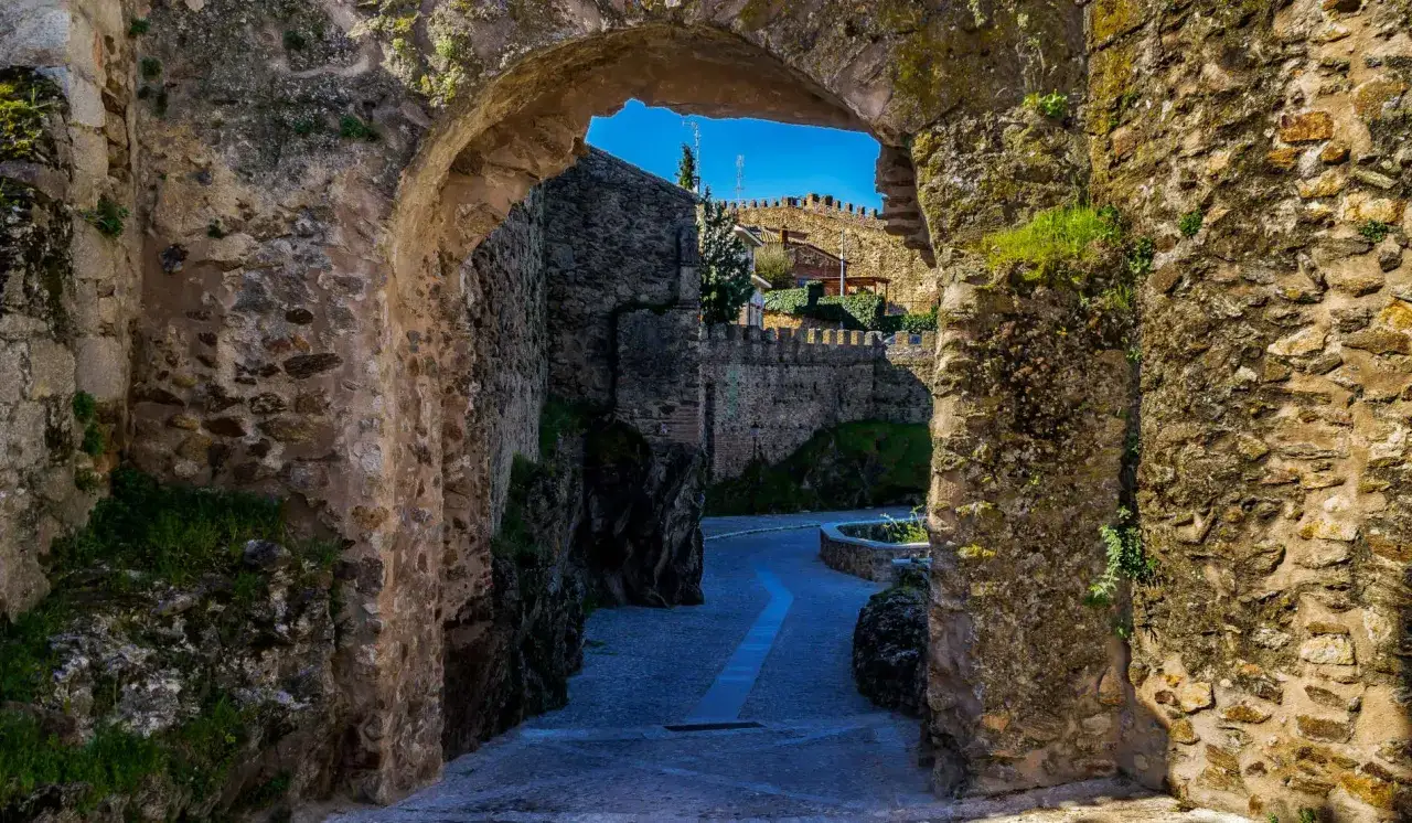 Un arco de piedra revela un camino empedrado y murallas antiguas, ideal para una escapada fin de semana cerca de Madrid.