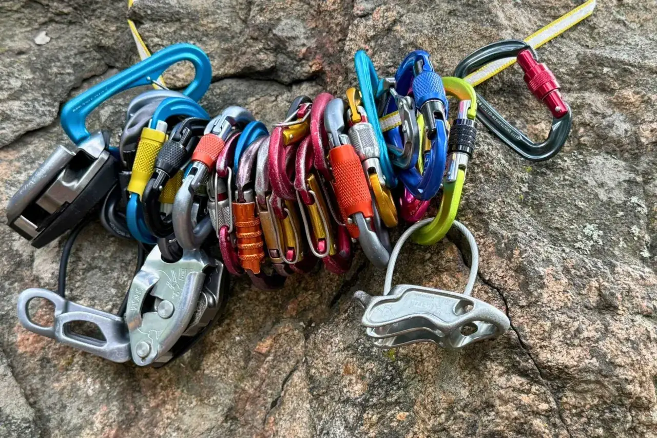 Un conjunto de mosquetones de escalada de colores vibrantes y dispositivos de aseguramiento descansan sobre una roca. Estos son los mejores mosquetones para tu pr&oacute;xima aventura.