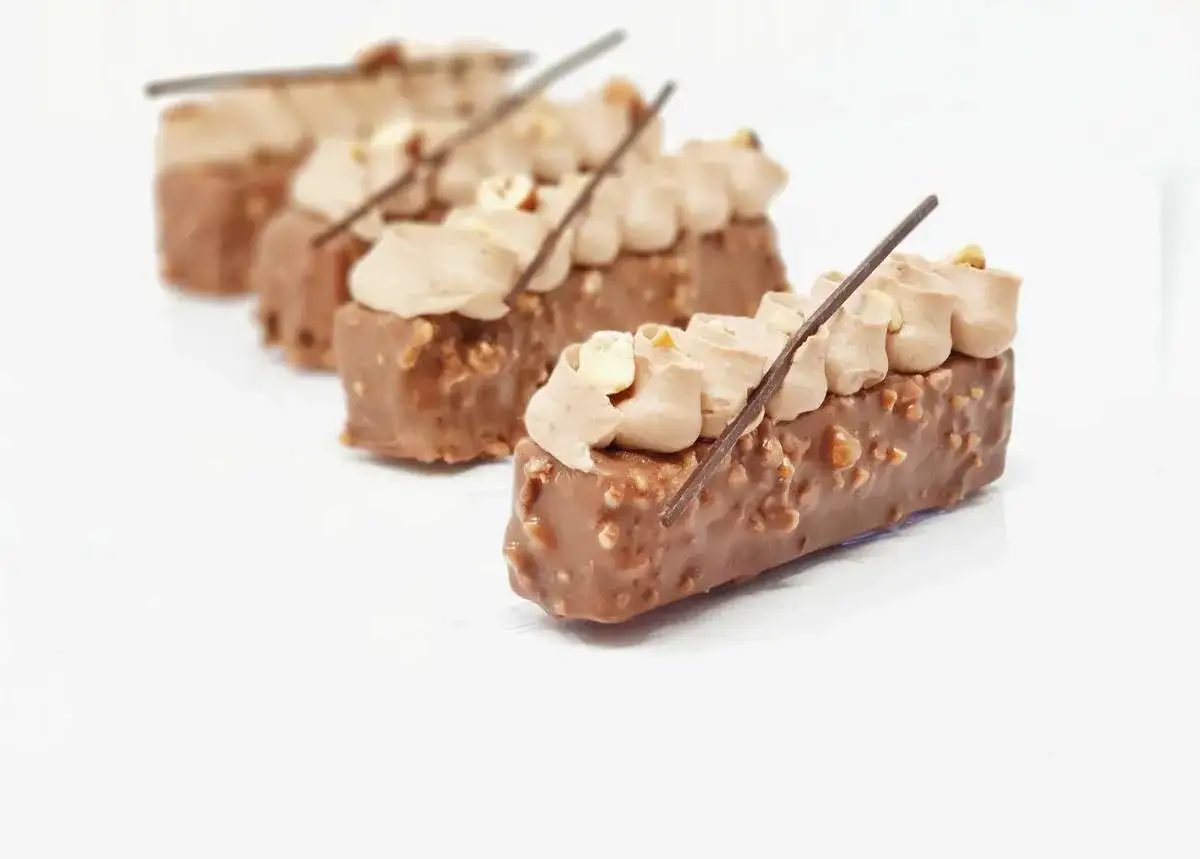 Délicieux rectangles de chocolat, parsemés de noisettes croquantes, surmontés d'une crème onctueuse et d'un bâtonnet de feuilletine. Un délice croustillant praliné feuilletine.
