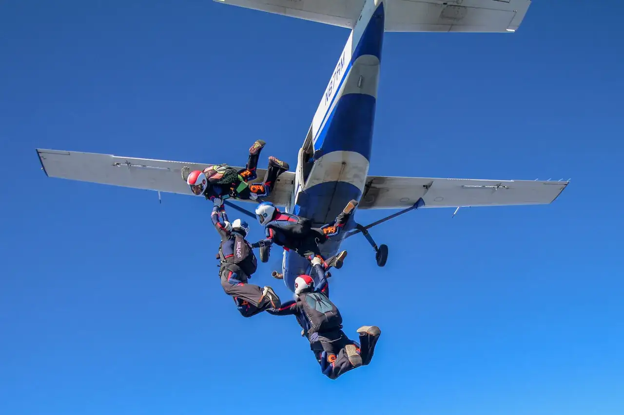 Vier Fallschirmspringer hängen am Flugzeug, bereit für ihren Sprung in den blauen Himmel.