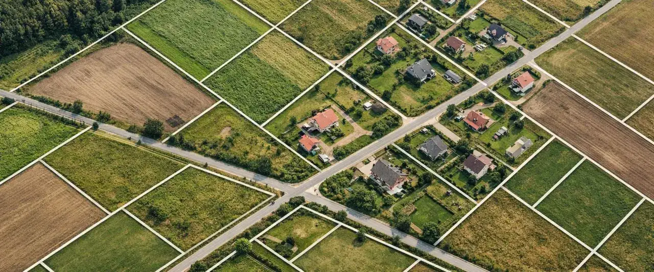 Działki budowlane podzielone białymi liniami, domy i pola. Kluczowe aspekty do rozważenia przy zakup działki budowlanej.