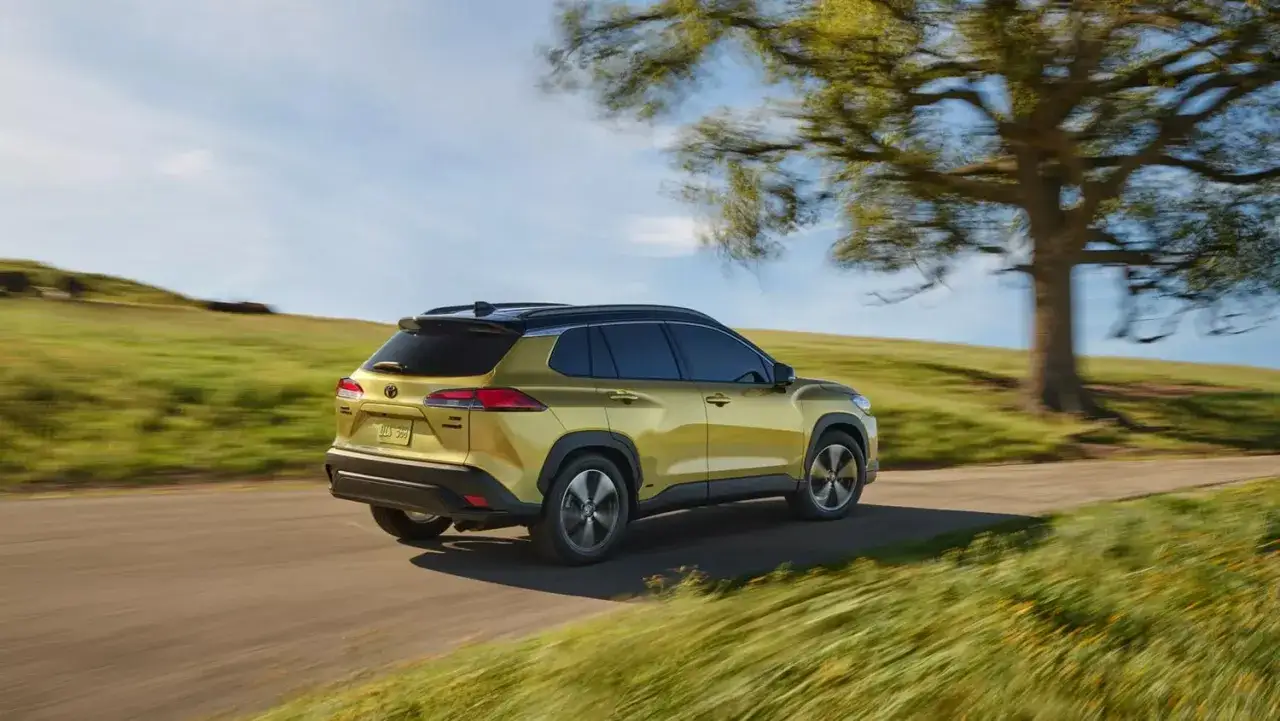 Złoty Toyota 2024 na krętej drodze wśród zielonych wzgórz.