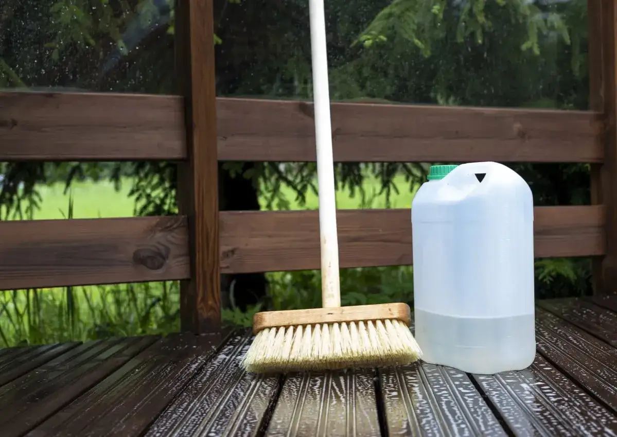 Brosse et bidon d'eau pour nettoyer terrasse pierre bicarbonate. Le bois est mouillé, prêt pour le nettoyage.