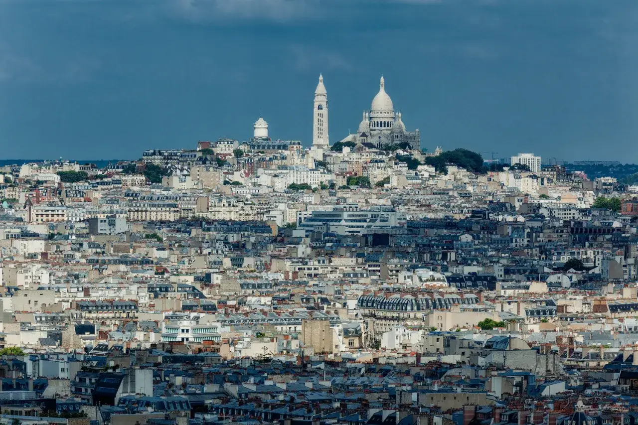 Paris bredvid Sacre Coeur, en vidsträckt vy över stadens takåsar under en dramatisk himmel.