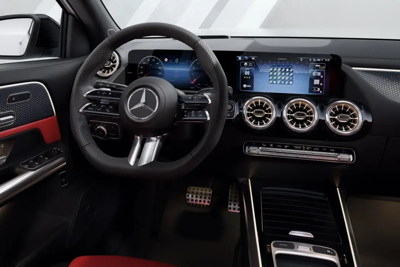 Interni moderni della nuova Mercedes GLA 2026: volante sportivo, doppio schermo digitale e dettagli rossi.