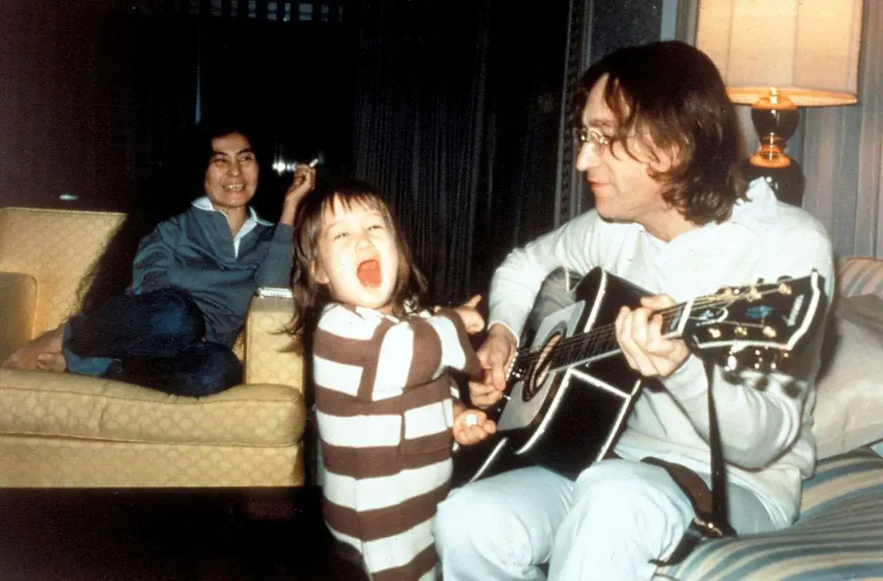 John Lennon III spielt Gitarre, w&auml;hrend Yoko Ono zusieht. Ein fr&ouml;hliches Kind in gestreiftem Pyjama singt laut mit.