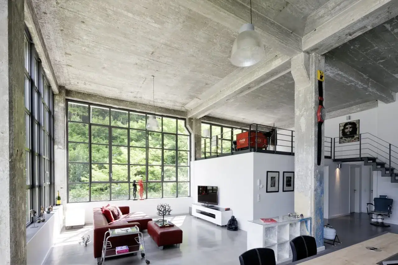 Offenes Wohnkonzept mit Betonwänden, großen Fenstern und einer Galerie – die loft definition in Perfektion. Rotes Sofa, moderne Treppe.