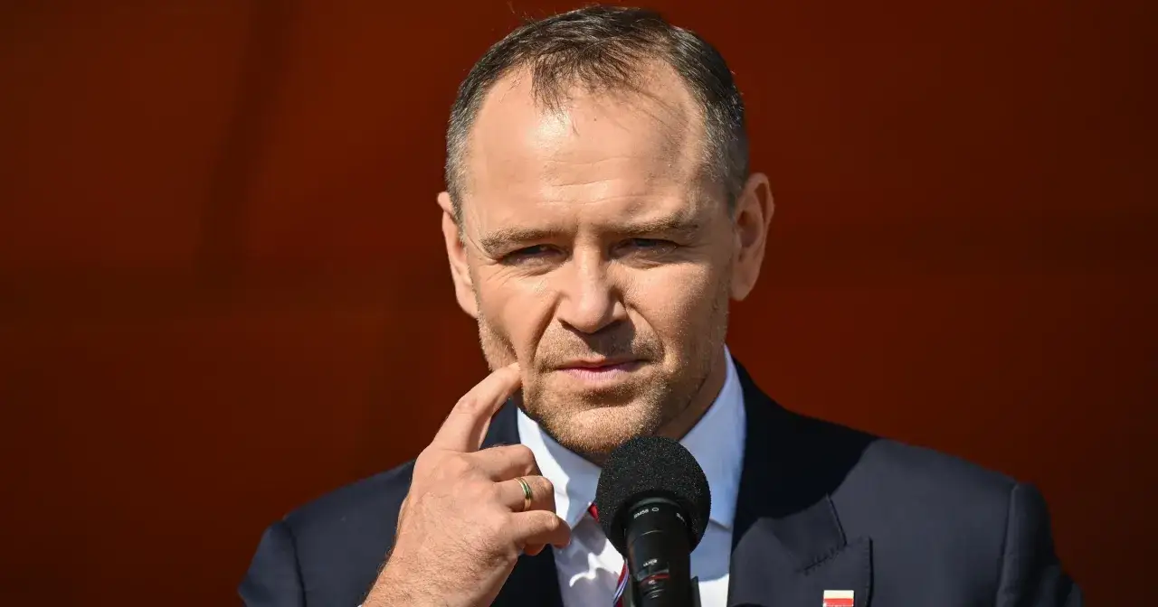 Mężczyzna w garniturze, z palcem przy policzku, zastanawia się, dlaczego urząd prezydenta jest uznawany za najdroższy w utrzymaniu w całej Europie Środkowej.