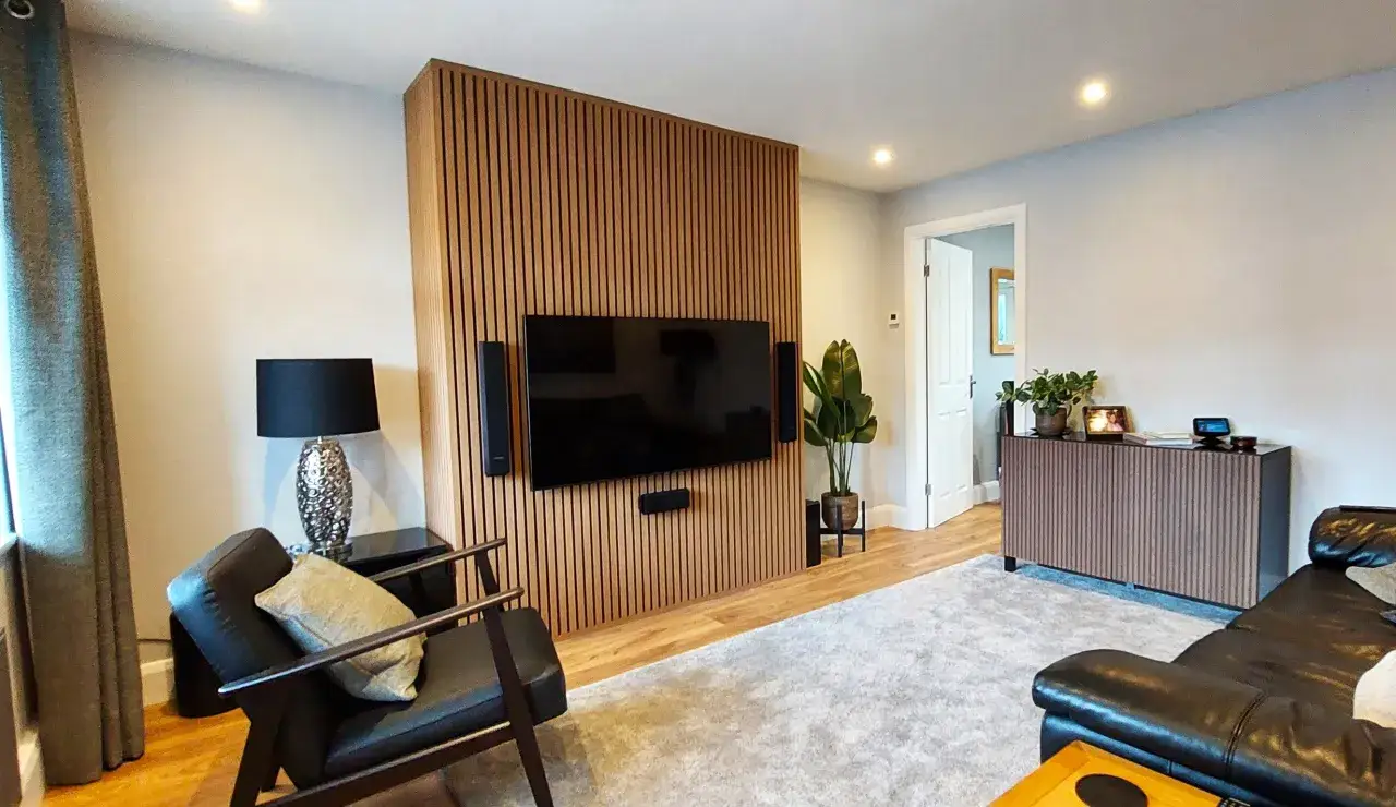 Modernes Wohnzimmer mit einem eleganten TV-Wand-Design. Die vertikalen Holzlamellen schaffen eine warme Atmosph&auml;re und integrieren den Fernseher nahtlos.