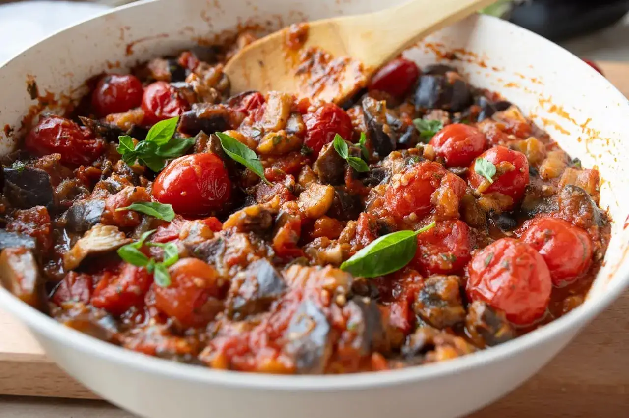 Un plat de caponata sicilienne mijot&eacute;, avec des aubergines, des tomates cerises et du basilic frais, pr&ecirc;t &agrave; &ecirc;tre d&eacute;gust&eacute;.