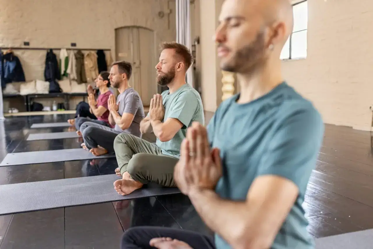 Män sitter på yogamattor i meditation, med händerna i böneställning. Namaste betyder
