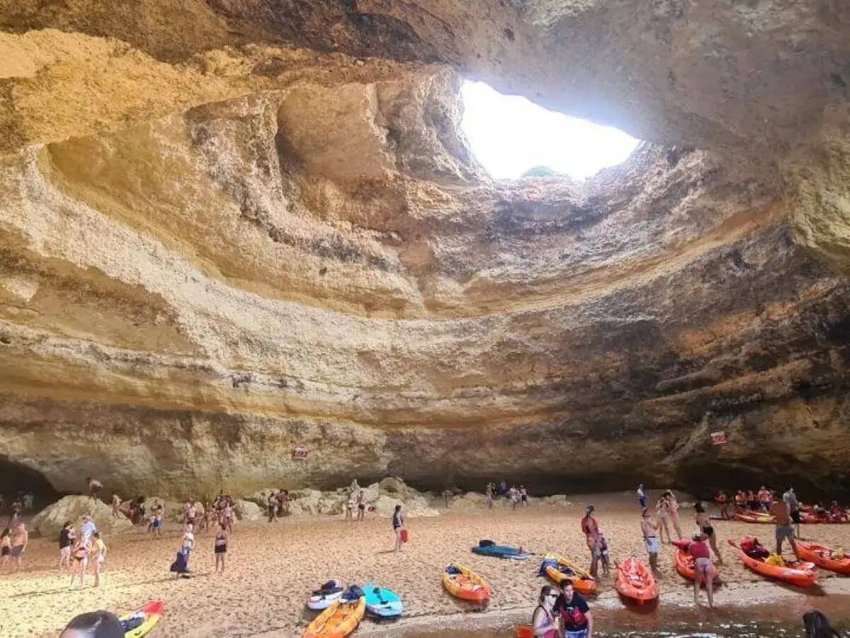 Gente disfrutando de actividades en el Algarve, como kayak, en una cueva con un agujero en el techo.