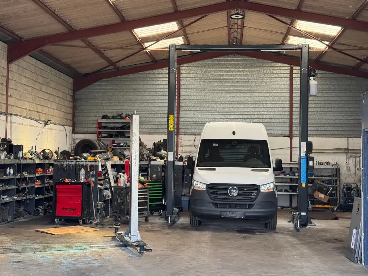 Un utilitaire blanc, un utilitaire sans AdBlue, est prêt pour la maintenance dans un garage. Des outils et des pièces sont rangés sur les étagères.
