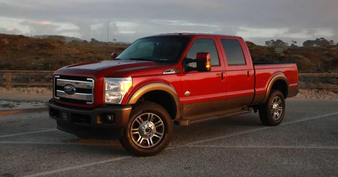 Czerwony Ford F350 King Ranch z brązowym pasem, zaparkowany na tle wzgórz i nieba o zachodzie słońca.