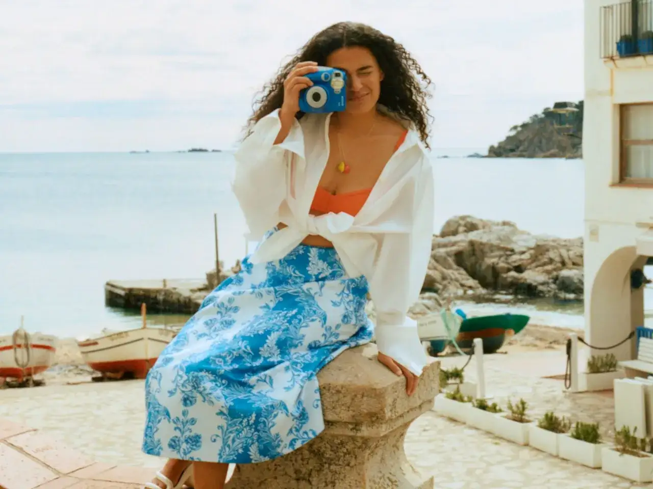 Mujer con cámara azul captura la esencia de viajar sola en un pintoresco pueblo costero.
