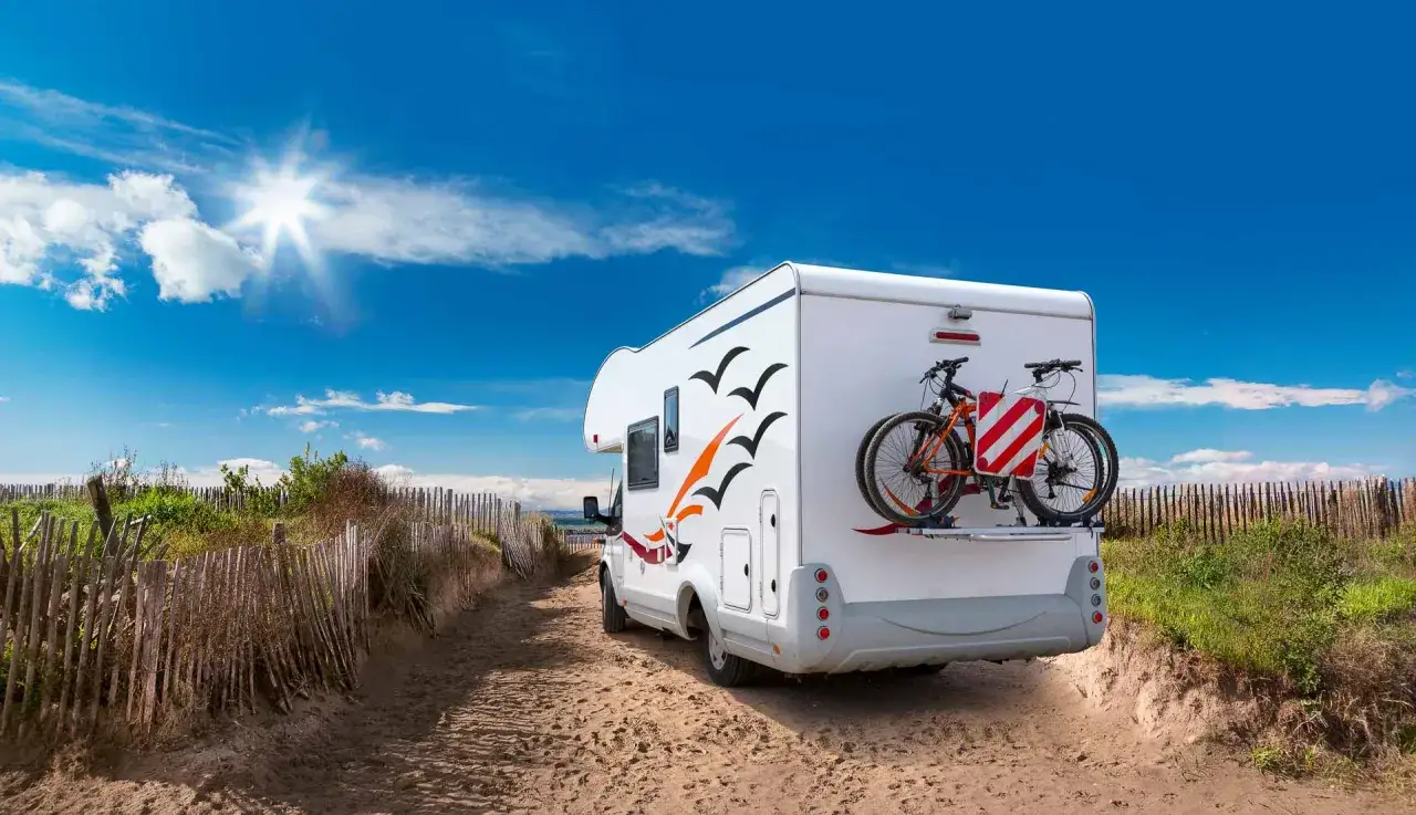 Camping-car prêt pour l'aventure sur une aire de camping-car à l'Île de Ré, avec vélos à l'arrière, sous un ciel bleu éclatant.