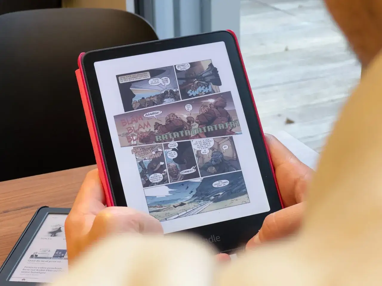 Une personne lit une bande dessinée d'action sur sa liseuse Kindle. Les bulles de dialogue