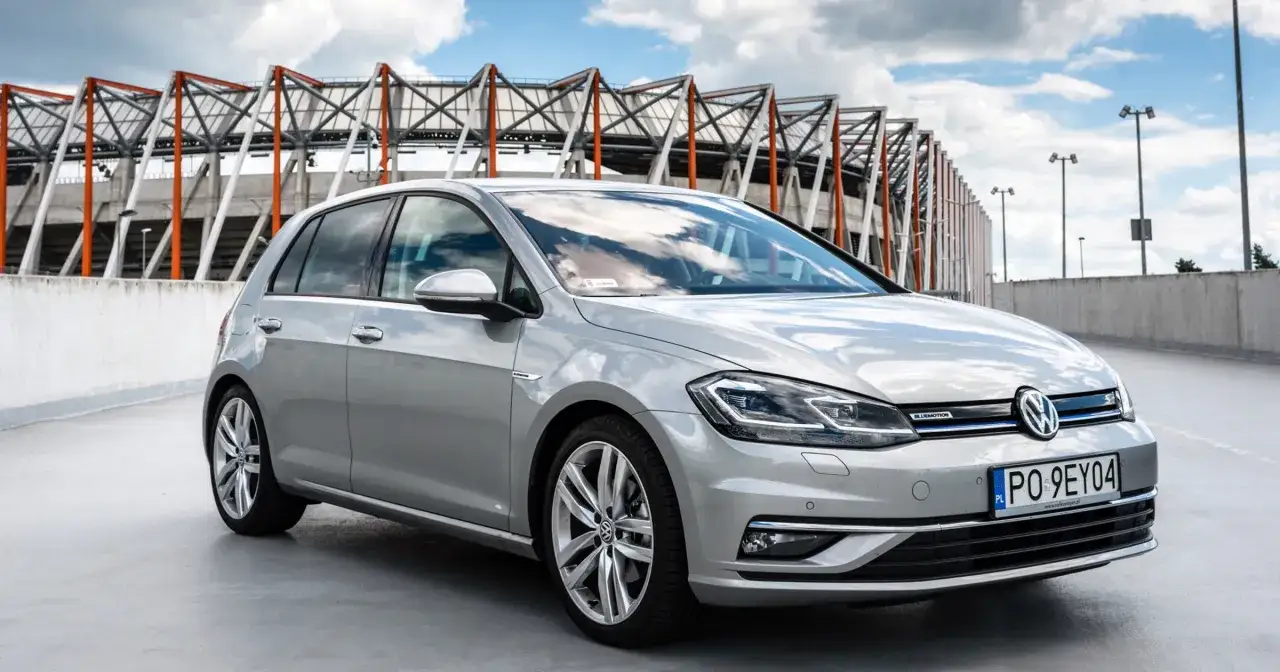 Srebrny Volkswagen Golf z technologią Bluemotion, co to jest? To oszczędność paliwa i ekologia w jednym. Auto stoi na tle stadionu.