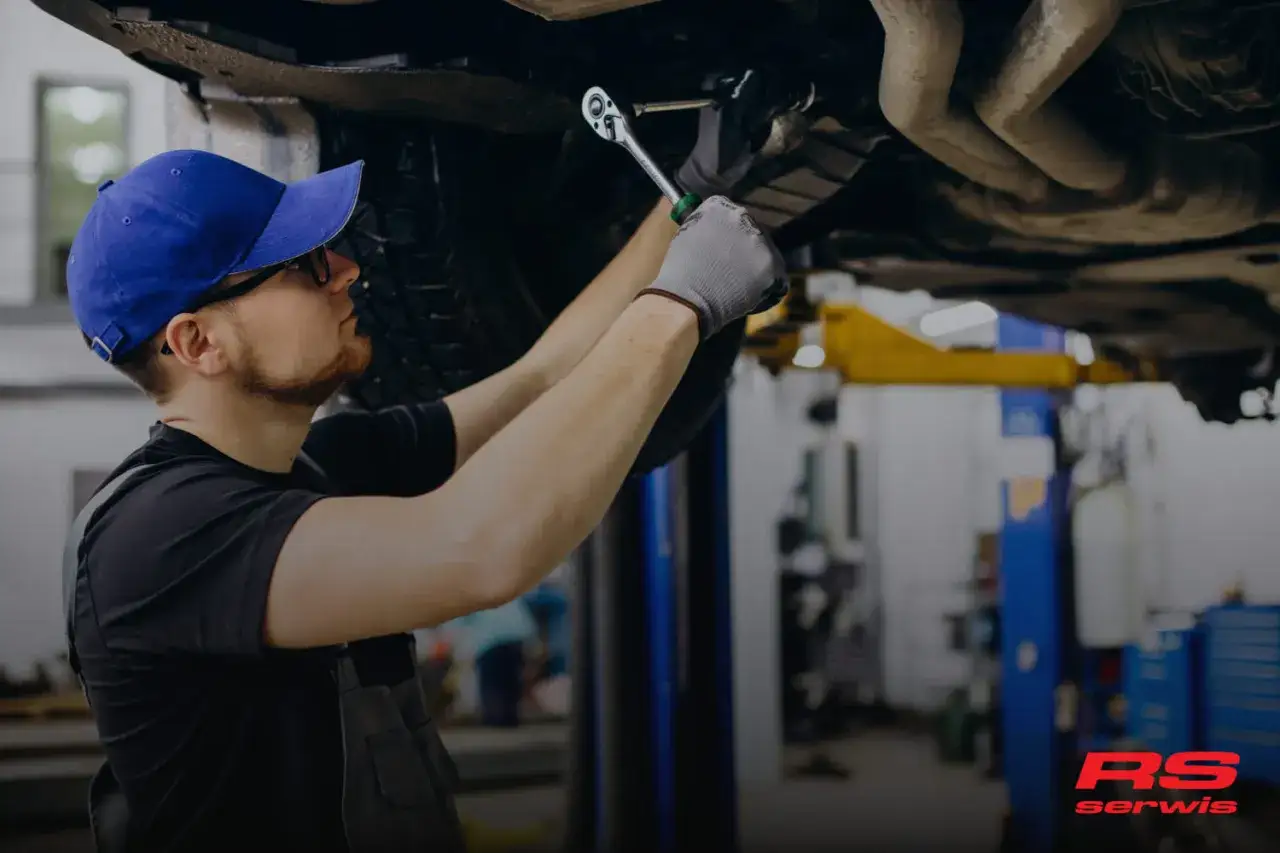 Mechanik w warsztacie naprawia uszkodzenie elementów układu nośnego samochodu, używając klucza nasadowego.