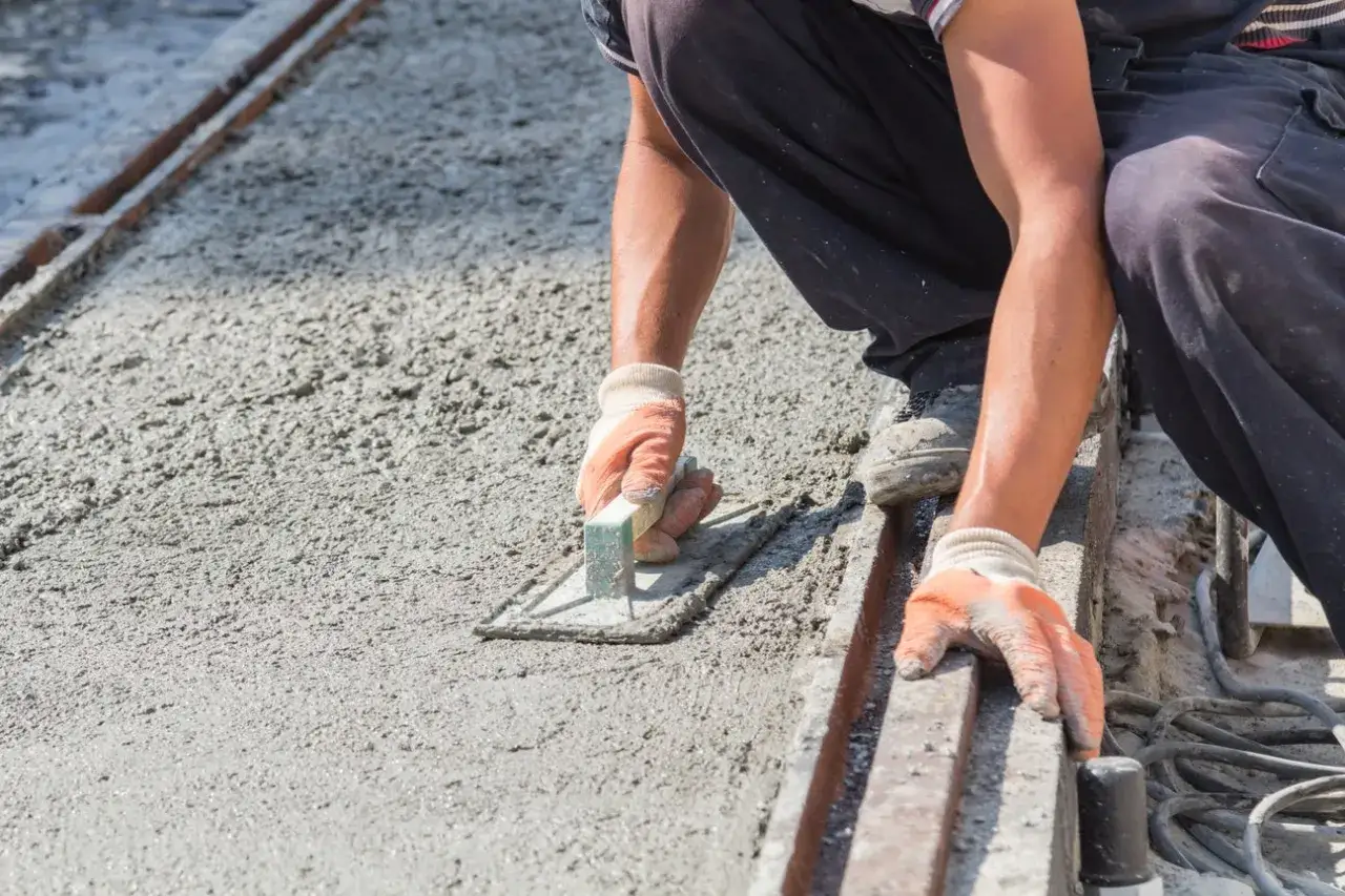 Pracownik w rękawiczkach wygładza świeży beton kielnią. Kluczowe są odpowiednie suchy beton proporcje dla trwałej nawierzchni.