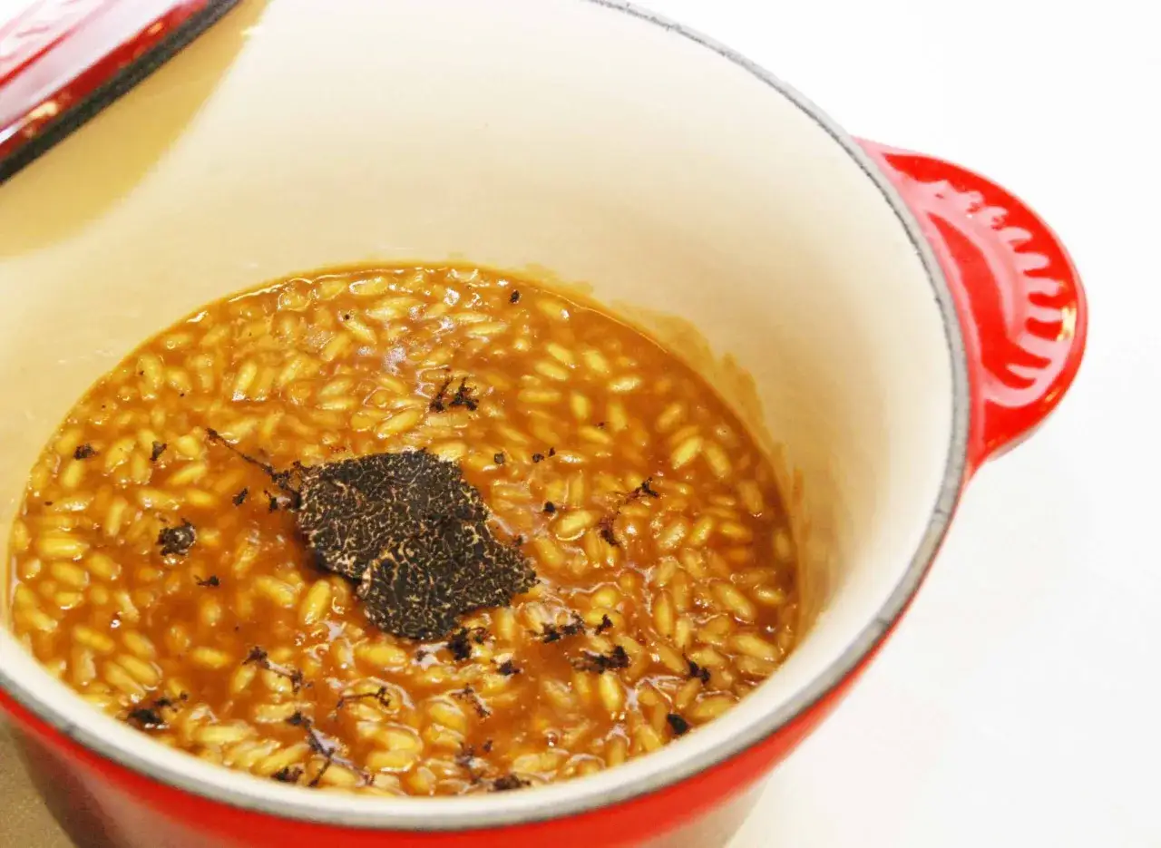Arroz a la milanesa cremoso con láminas de trufa negra en una olla roja.
