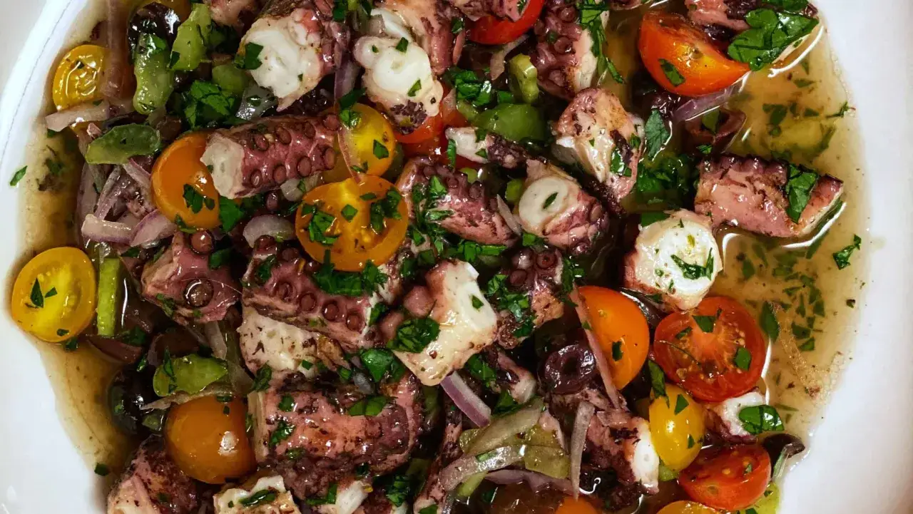 Oktopus Salat mit Kirschtomaten, roten Zwiebeln und Oliven in einer leichten Vinaigrette.
