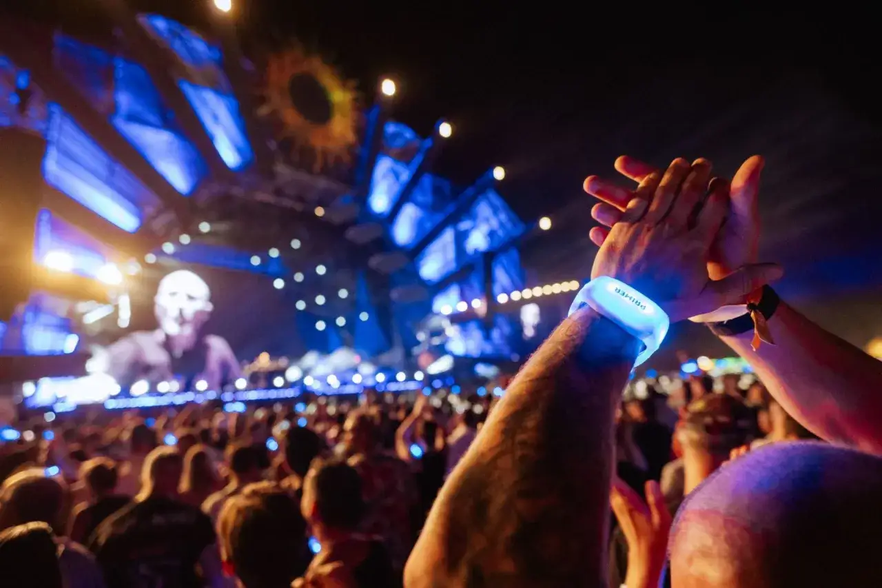 Pubblico in delirio a un concerto, con braccialetti luminosi che pulsano al ritmo delle canzoni inglesi famose moderne.