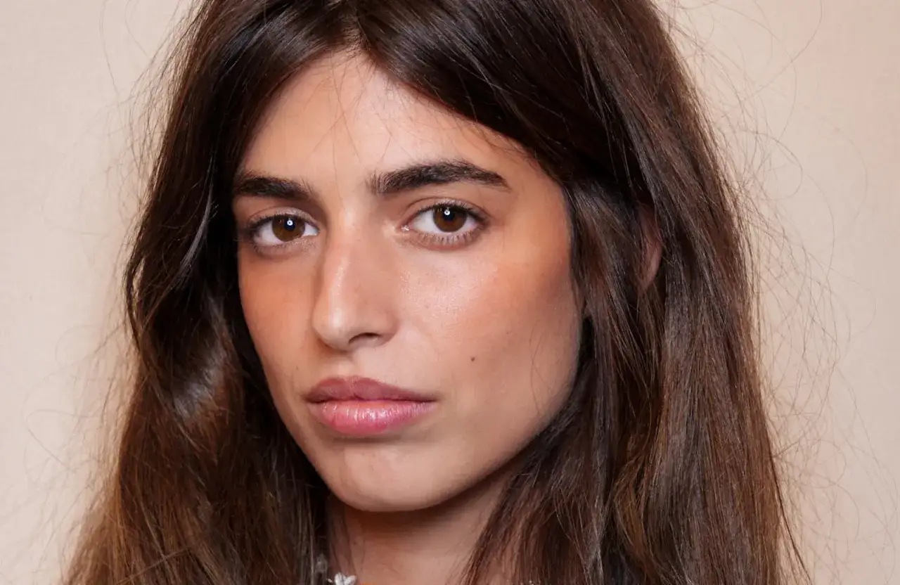 Portrait d'une jeune femme aux longs cheveux bruns. Son regard est intense, souligné par un maquillage naturel et un sourcil poil à poil parfaitement dessiné.