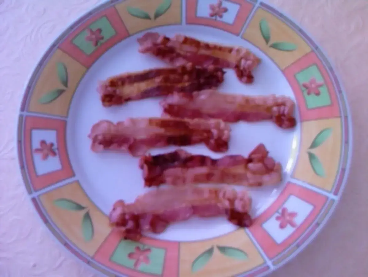 Knuspriger Bacon, schnell in der Mikrowelle zubereitet, liegt auf einem Teller mit Blumenmuster.