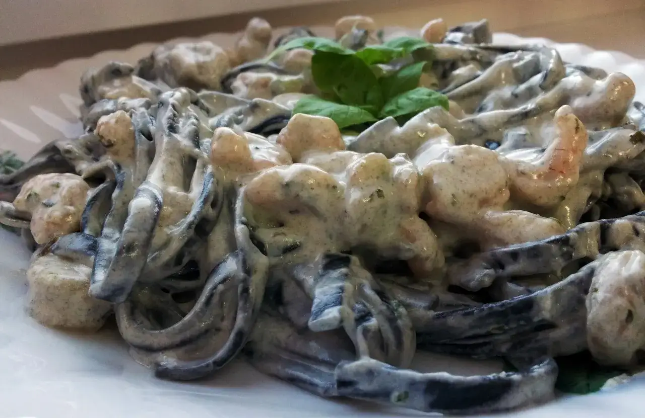 Pyszne dania z krewetkami: czarny makaron tagliatelle w kremowym sosie z kawałkami krewetek i listkami bazylii.