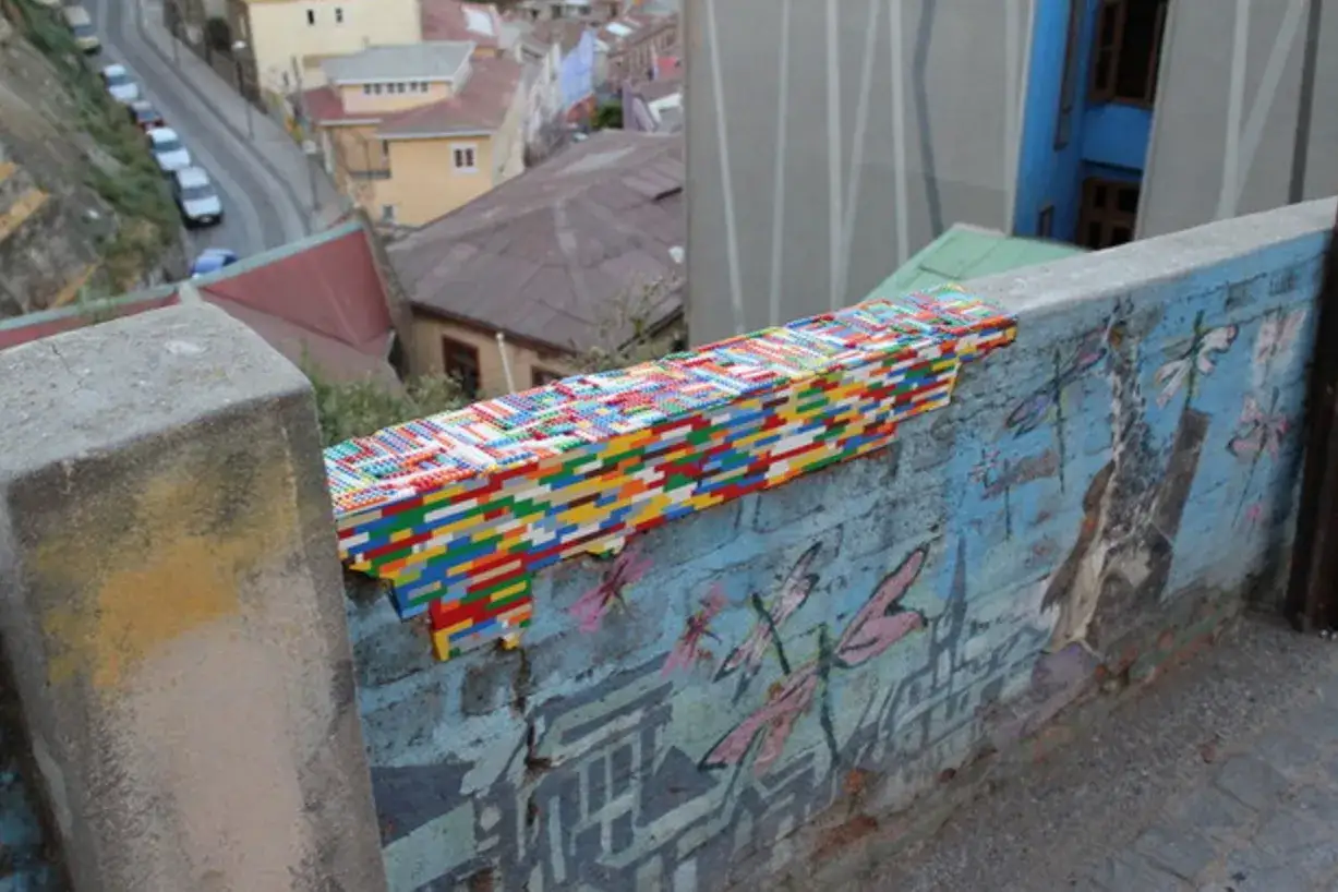 Un muro con un graffito di libellule e un'installazione colorata di mattoncini Lego, un'idea creativa per coprire una crepa nel muro.