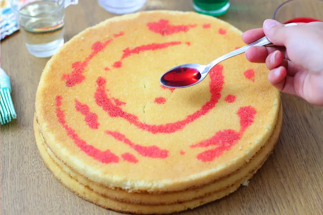 Un cucchiaino di sciroppo rosso viene versato su un pan di spagna decorato con un motivo a spirale. La bagna per pan di spagna renderà la torta più umida e gustosa.