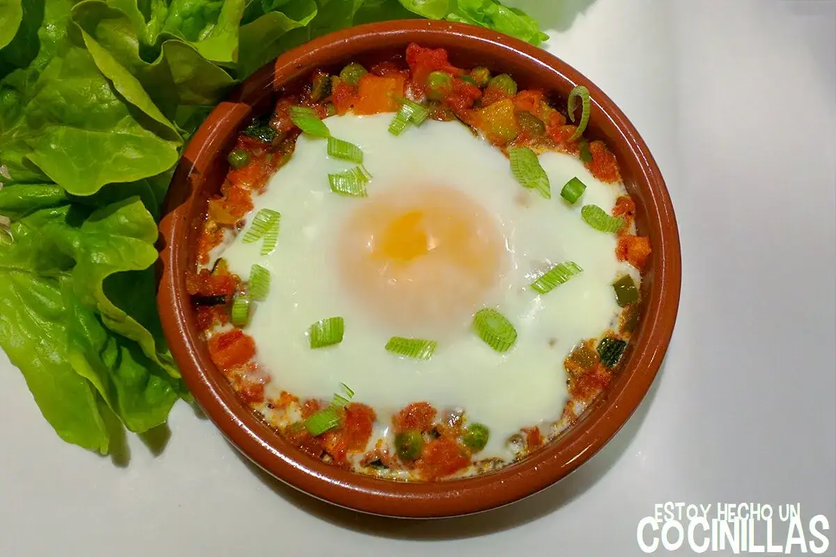 Un huevo escalfado sobre un sofrito de verduras, con cebolleta picada. Un plato que recuerda al hervido valenciano, acompañado de hojas de lechuga fresca.