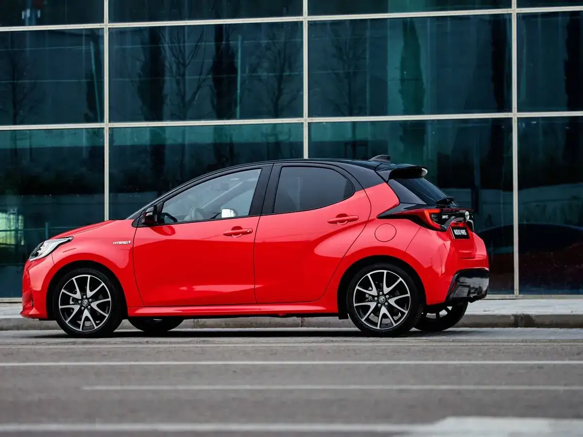 Un Toyota Yaris rojo, &aacute;gil como caballos salvajes, se detiene frente a un edificio moderno.