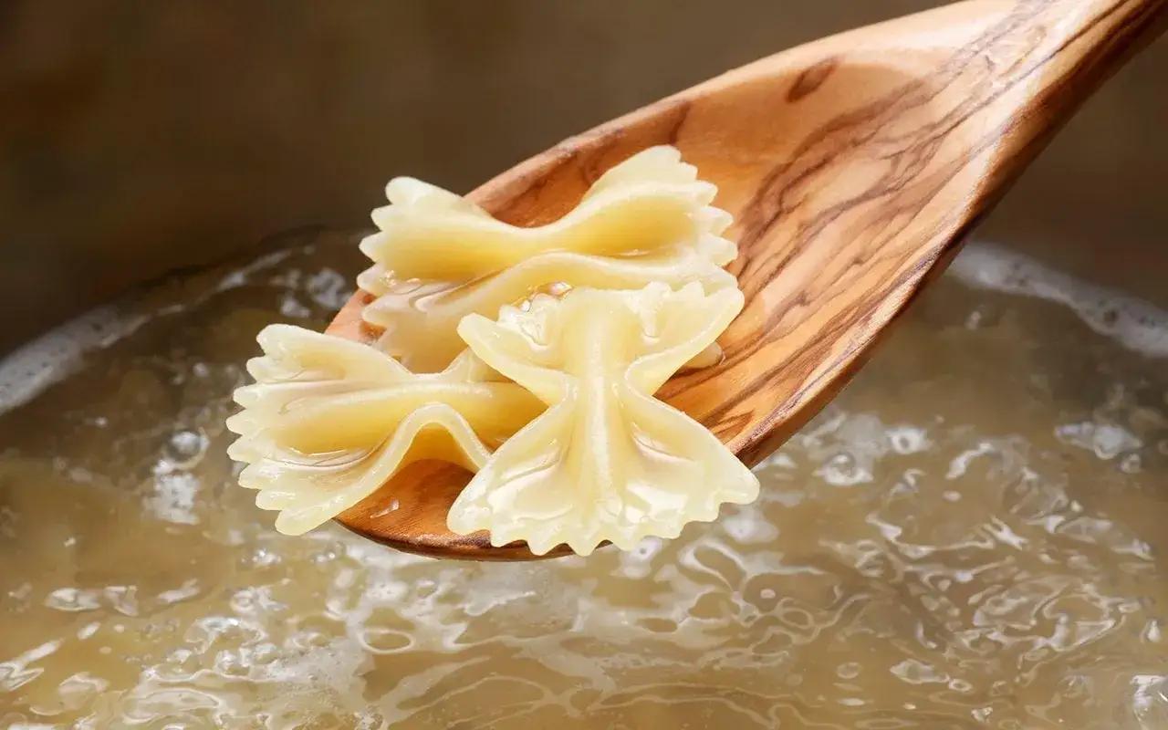 Holzkochl&ouml;ffel mit Farfalle-Nudeln &uuml;ber kochendem Wasser. Die perfekte Farfalle Kochzeit ist fast erreicht.