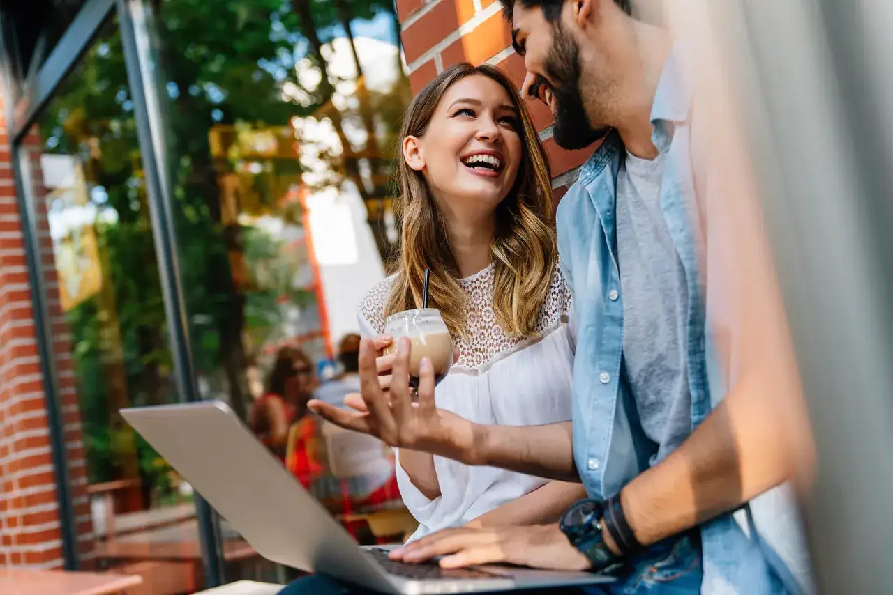 Coppia sorridente con un caffè e un laptop, un'immagine che cattura la loro affinità di coppia e la complicità.