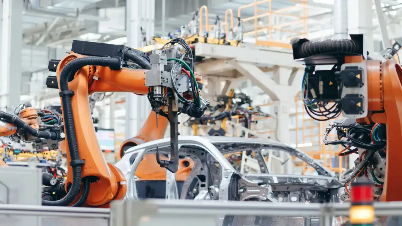 Roboty przemysłowe pracują nad karoserią samochodu. To idealne miejsce na audyt sprężonego powietrza, by zapewnić płynność produkcji.