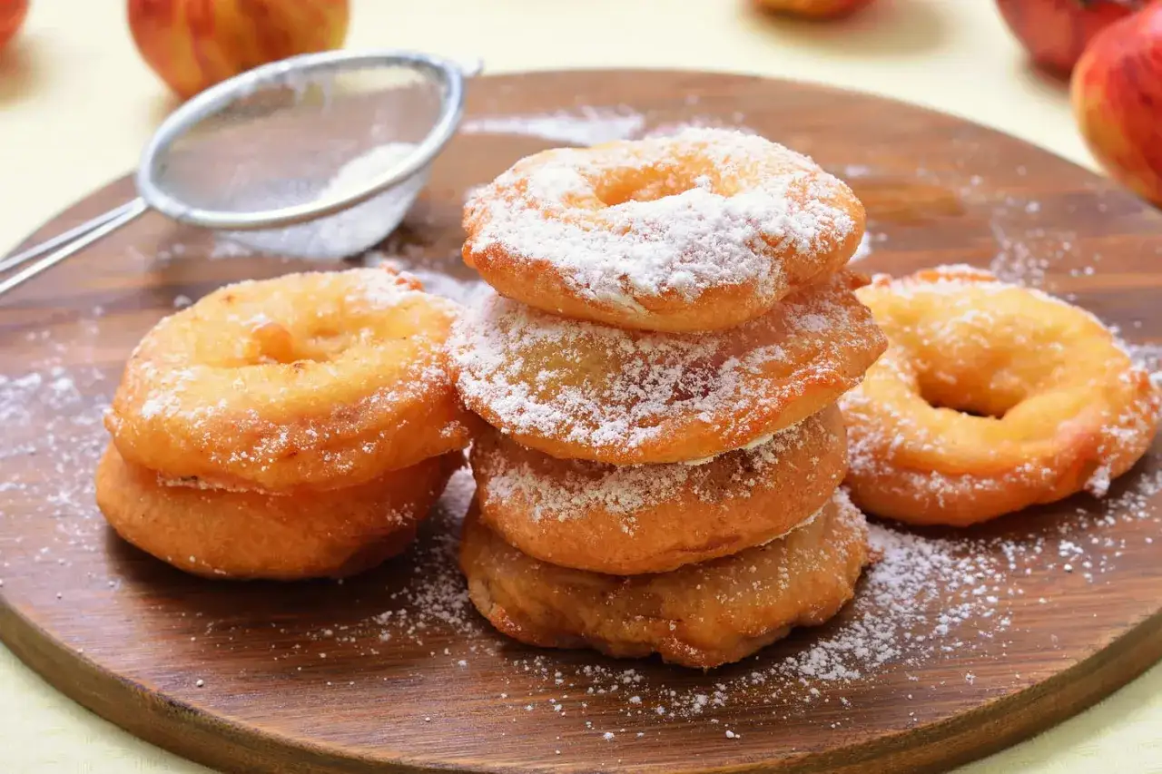 Pile de beignets aux pommes saupoudrés de sucre glace, prêts à être dégustés.