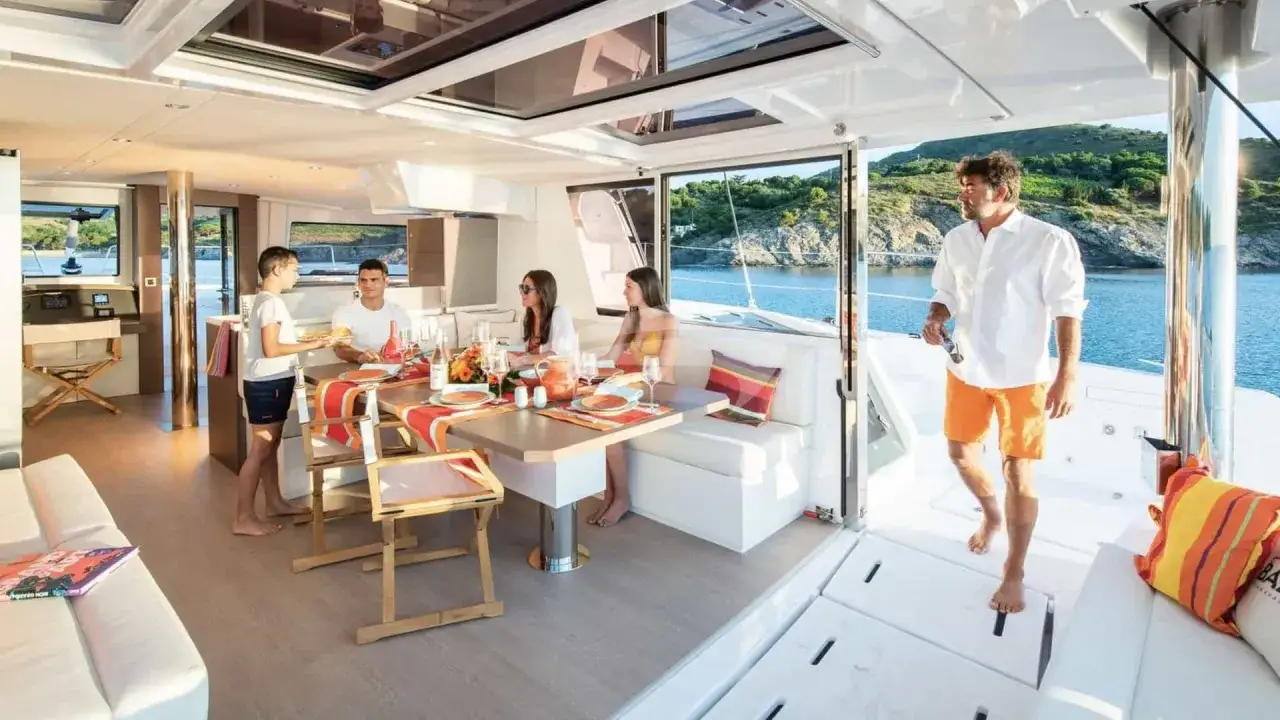 Interni del Koru yacht: famiglia riunita per pranzo, con vista mare e colline verdi.