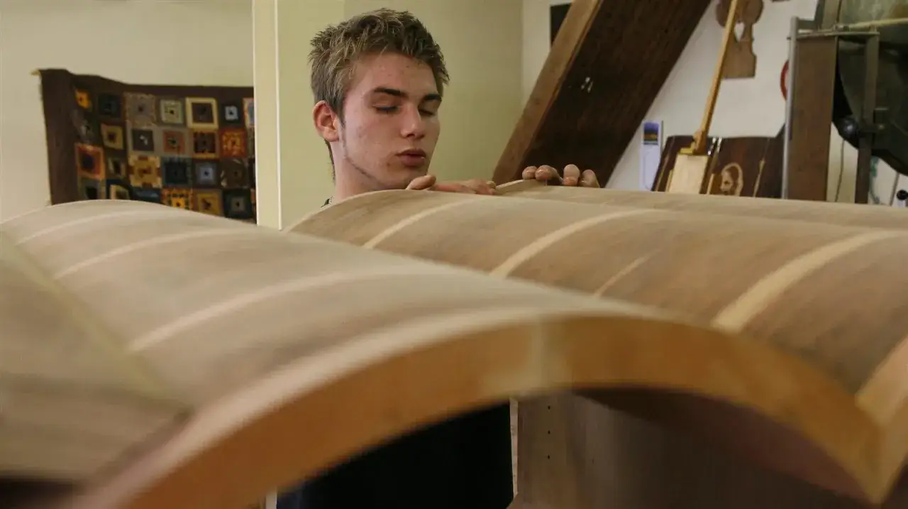 Un jeune homme apprend l'artisanat du bois, manipulant avec soin des pièces courbées.