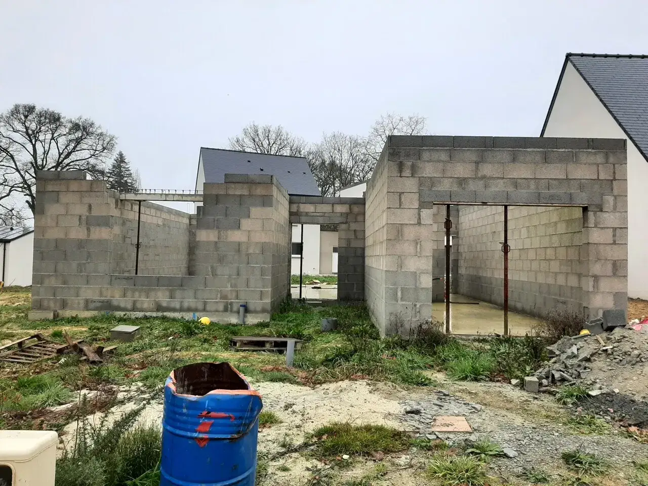 Chantier de construction : murs en parpaings, **travaux non finis**, un baril bleu rouillé au premier plan. Le **paiement** est en attente.