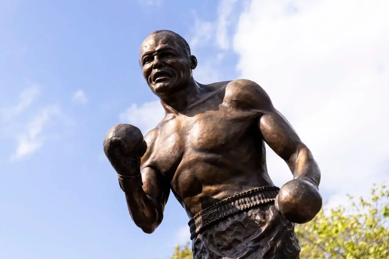 Bronze statue of boxer Jersey Joe Walcott in a fighting stance against a blue sky with clouds.