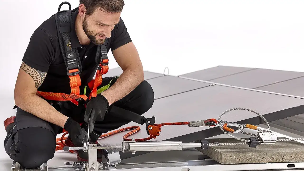 Mann mit Auffanggurt prüft ein seilsicherungssystem flachdach. Sicherheit bei der Montage von Solarmodulen.