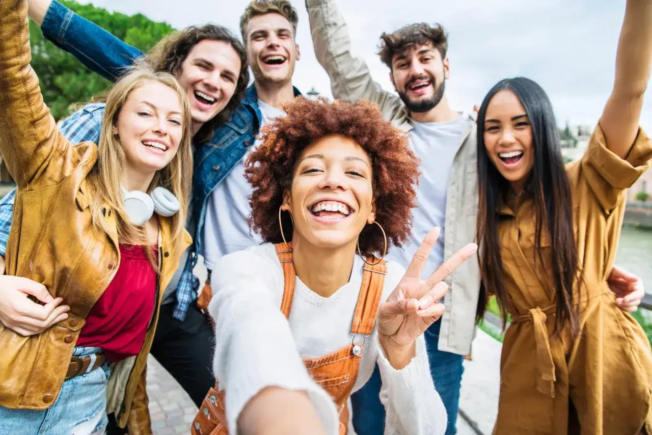Grupa przyjaciół robi selfie, śmiejąc się i pozdrawiając. To jest właśnie co to jest przyjaźń – radość i wspólne chwile.