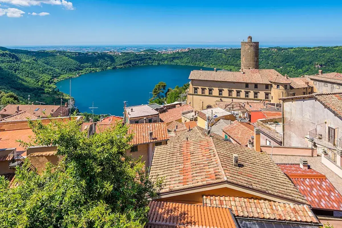 Vista panoramica di un borgo con tetti rossi affacciato su un lago blu, uno dei tanti **paesi da vedere vicino Roma** per una gita fuori porta.